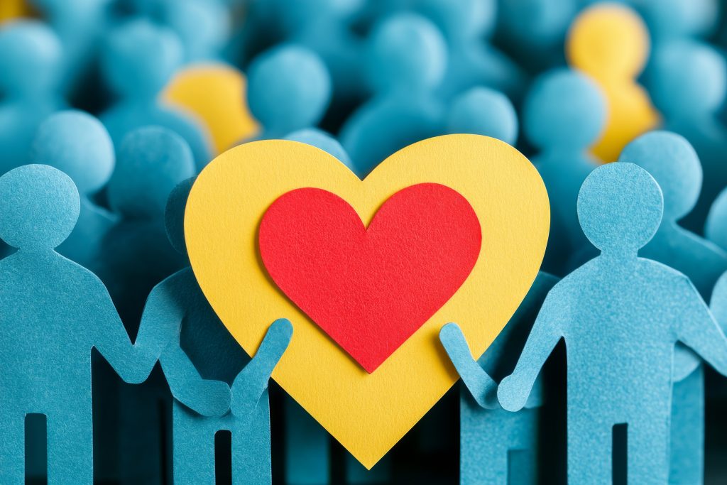 A group of people holding up paper cut outs with a heart.