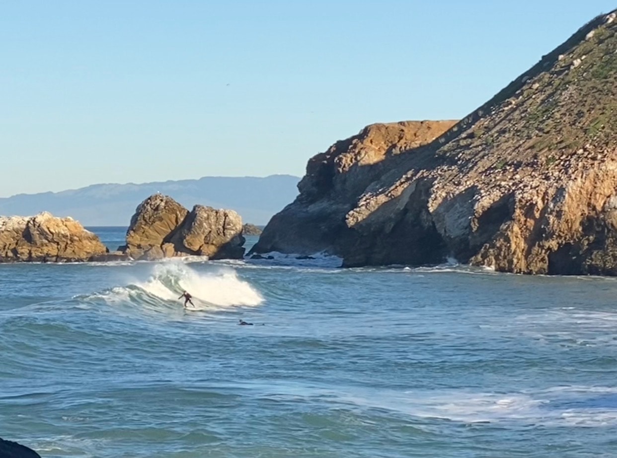 Surfer riding a wave beside the Pacifica cliffs